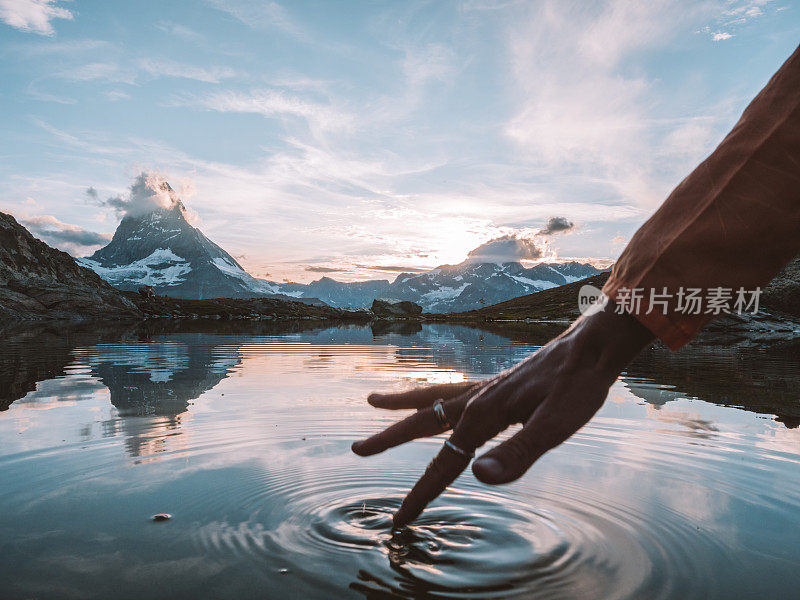 女性的手指触摸水面从高山湖泊下面的马特洪峰