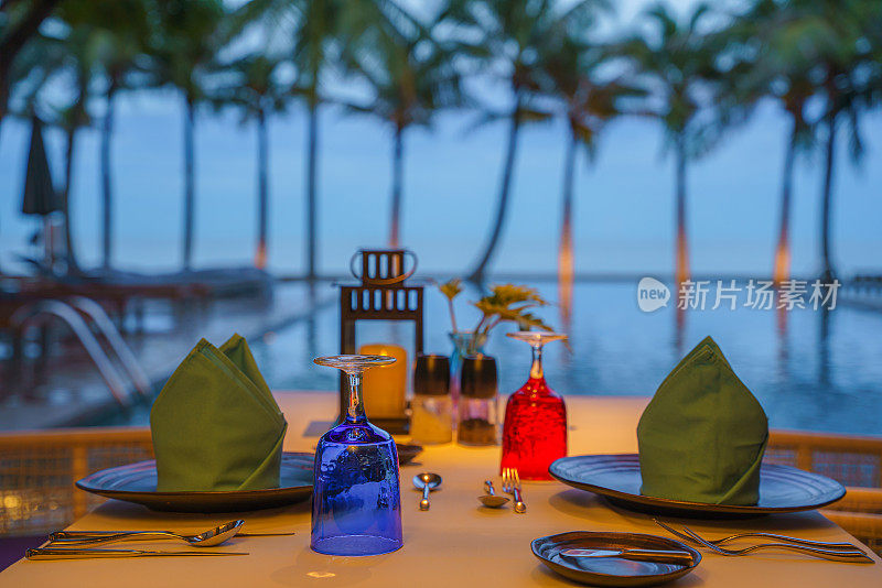 餐桌上的餐具和餐具准备晚餐在泳池边和海边的海滨精品度假村和酒店与日落天空在泰国华欣