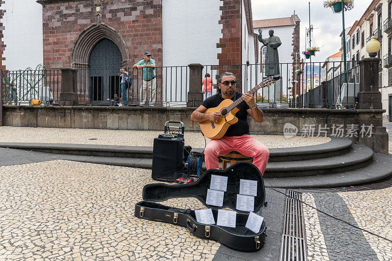 在葡萄牙马德拉岛的Funchal市中心，一名街头艺人在弹奏吉他