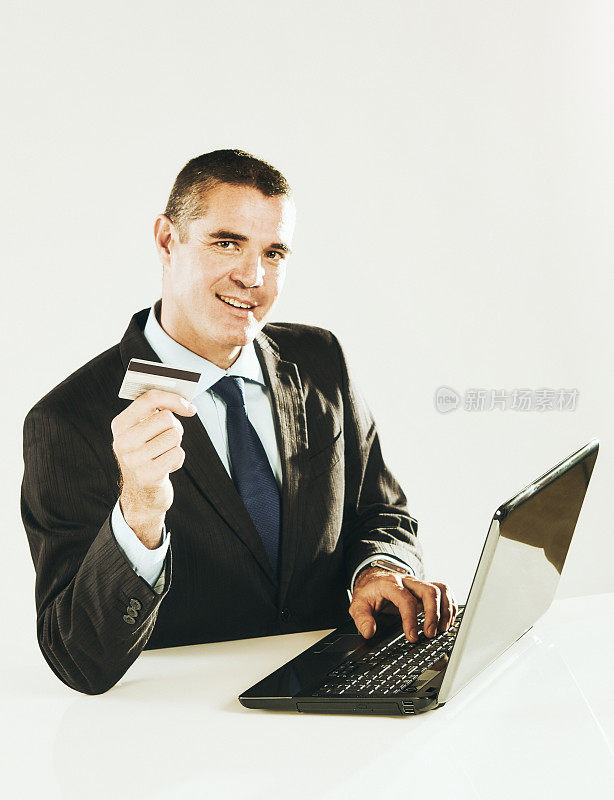 年近40的帅气男子手持信用卡坐在笔记本电脑前，看起来很自信