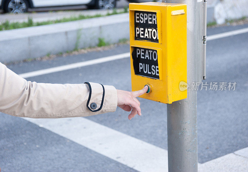 一个女人的手指按下了交通灯的行人按钮。出现的单词意思是:“等待行人”，“按行人”。