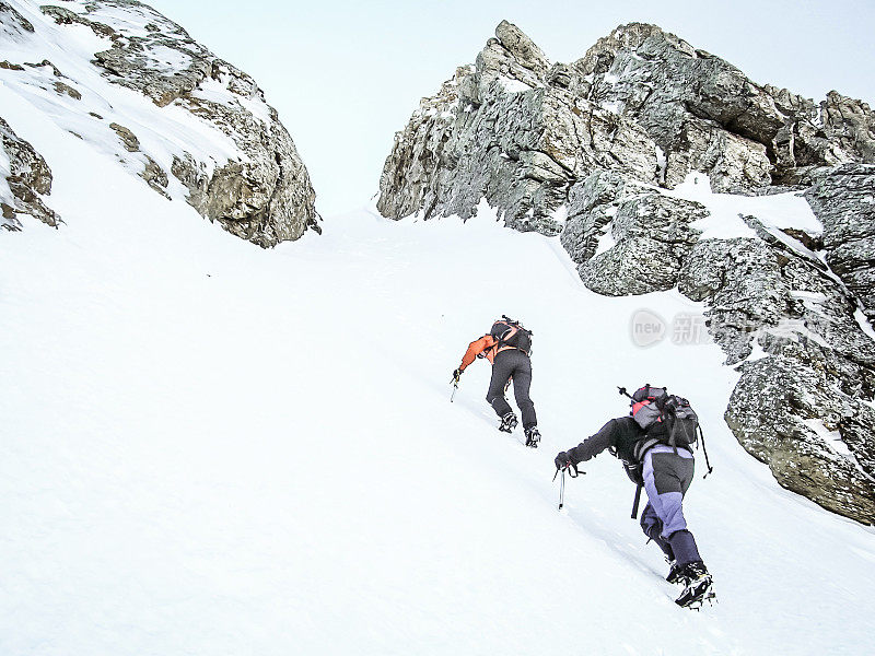 两个人用冰爪和冰斧攀登雪山的后视图。