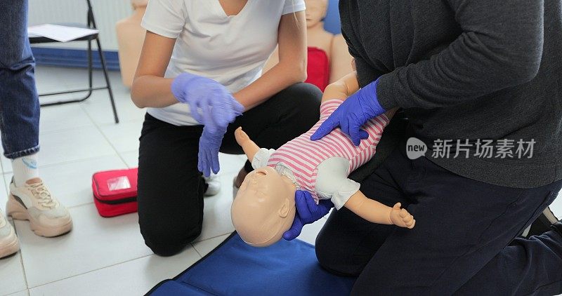 在室内急救小组训练中，一名男子正在学习如何对婴儿假人进行胸部按压。