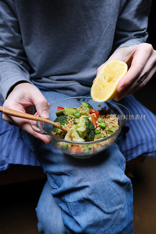 一个人在膝盖上把柠檬挤进一碗碾碎的干小麦和蔬菜里