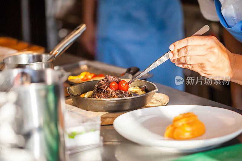 豪华酒店或餐厅厨房装饰盘厨师手特写。准备牛排，装饰菜。现代厨房及厨具