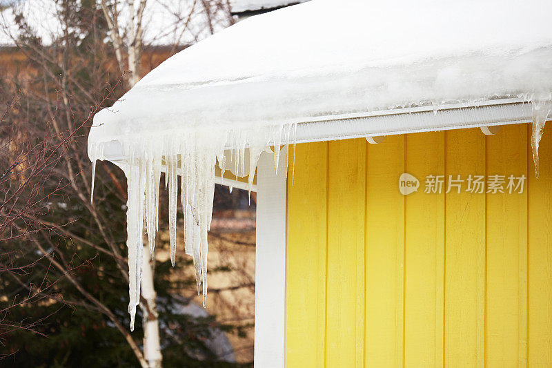 房子的屋顶有冰冻的雪，冰柱，黄色的墙在冬天