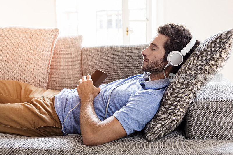 一个男人在沙发上用智能手机听音乐