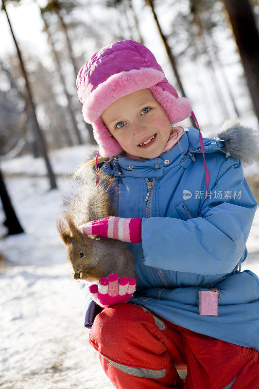 小女孩在冬天的森林里喂松鼠。