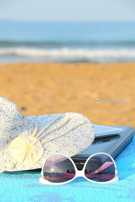笔记本电脑，太阳帽和太阳镜在海滩上