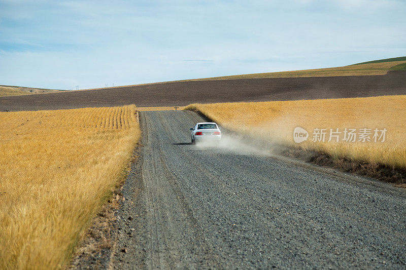 一辆白色的汽车在砂砾的农场道路上扬起一片尘土