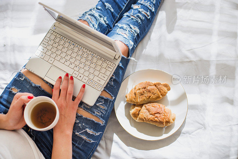 一个女人一边在床上吃早餐一边用笔记本电脑工作