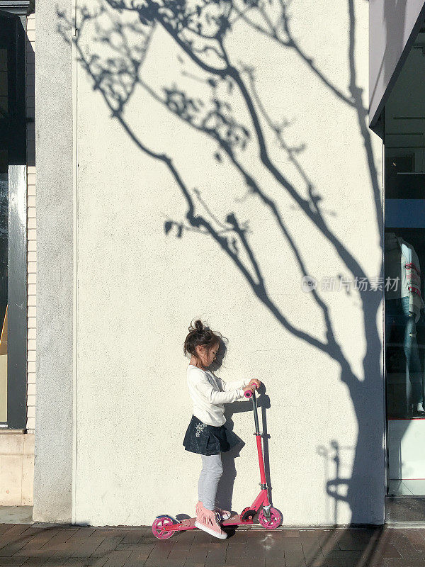 小女孩在人行道上推着她的摩托车