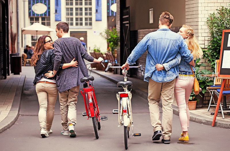 两对年轻夫妇在城市里散步，他们拿着自行车