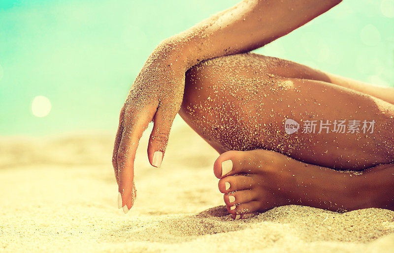 女人的手正躺在被海沙覆盖的膝盖上。