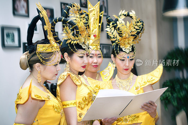 四位亚洲女演员穿着泰国传统的黄色服装读着空白的课本