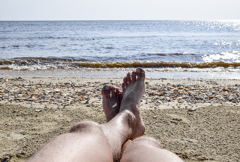 沙滩上一个男人的腿。一个男人躺在沙滩上休息。腿在框架里。