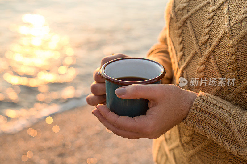 海边舒适的秋天。女人的手拿着一个盛着茶的杯子