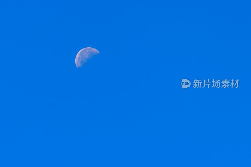 蓝色天空中的半月。明亮的月亮在晴朗的天空中环绕地球，在白天显示出陨石坑。给吉布斯打蜡过了第一节。南半球,冬天。