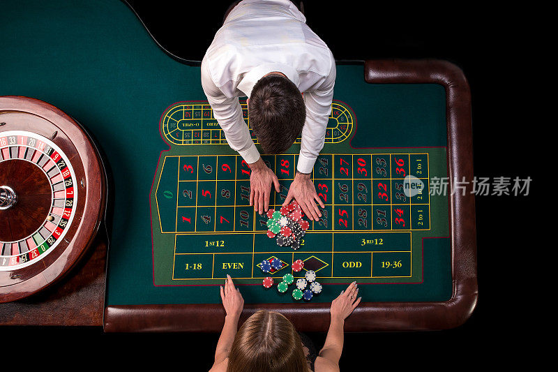 在赌场的桌子上玩轮盘赌的男人和女人。顶视图在轮盘赌绿色桌子与卷尺