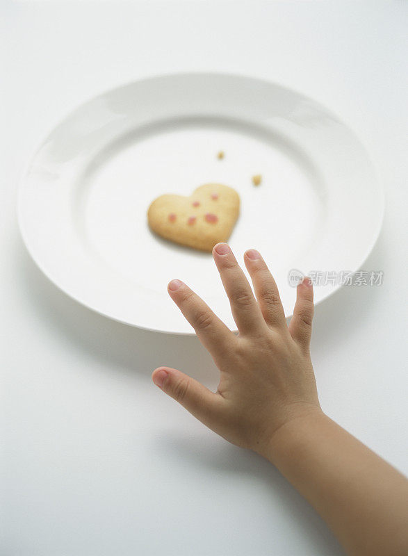 一个孩子的手伸向一个心形的饼干