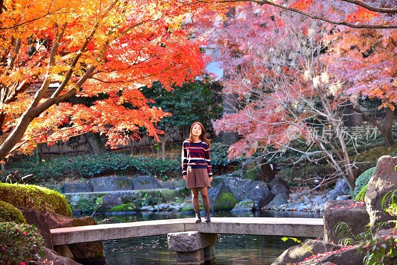 年轻的日本女子站在东京日本花园的石桥上