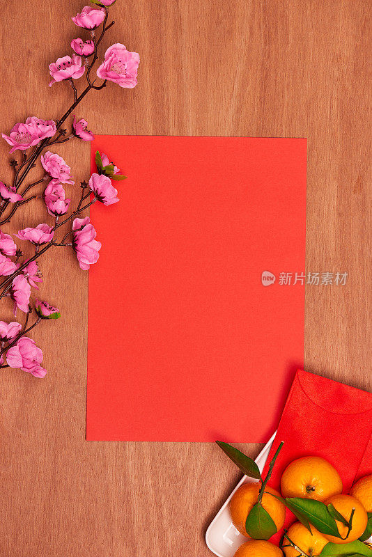 顶视图配件中国新年节日装饰。橙色，叶子，木篮子，红包，红色背景的梅花。