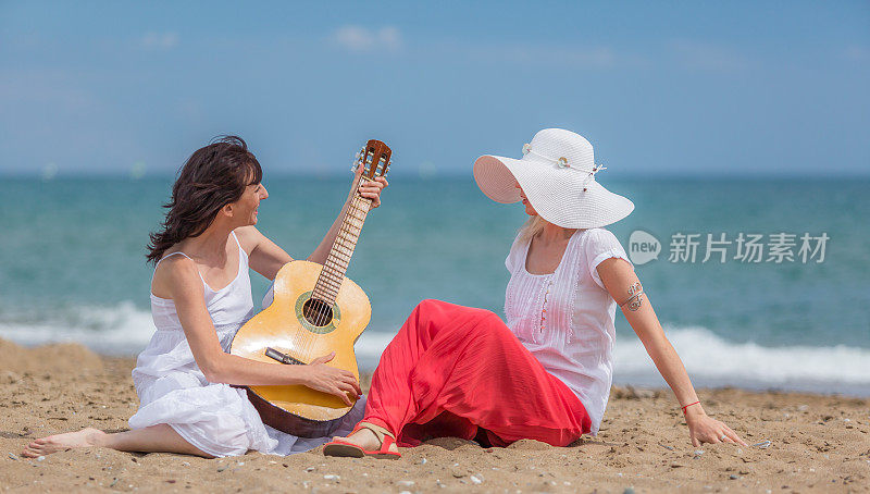 两个快乐的成熟女人微笑着在海滩上弹吉他