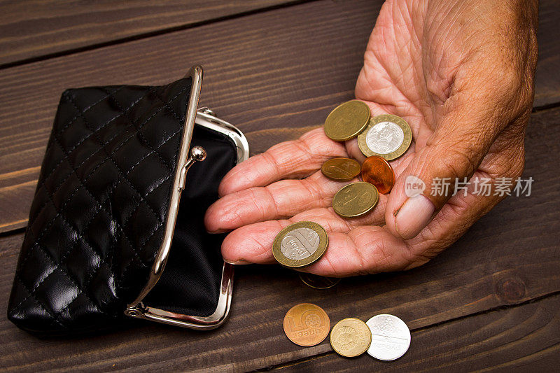 贫困。一个老人把硬币放在空空的旧皮夹上。退休后贫困的概念。