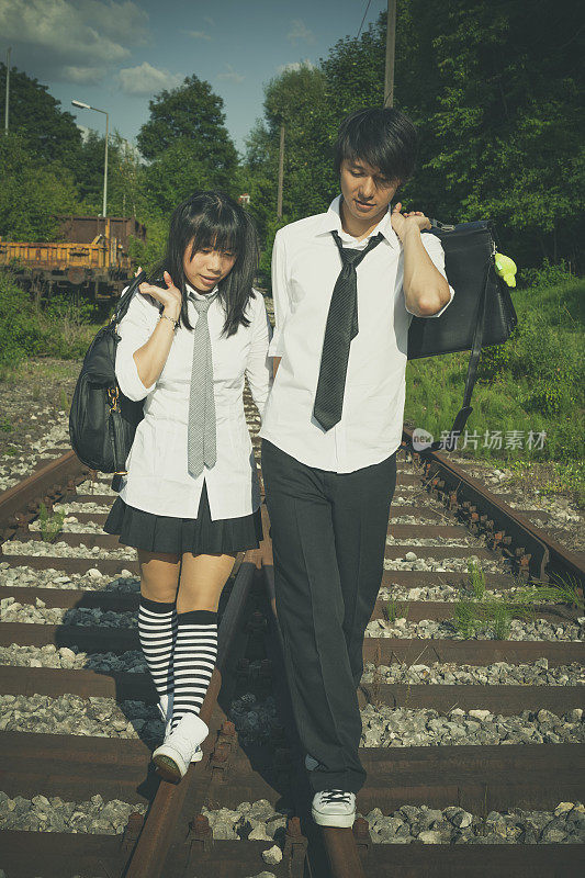 一对穿着校服的亚洲夫妇在铁轨上走回家