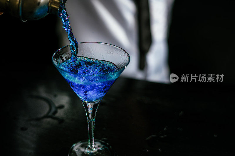 调酒师将蓝色鸡尾酒倒入马提尼酒杯