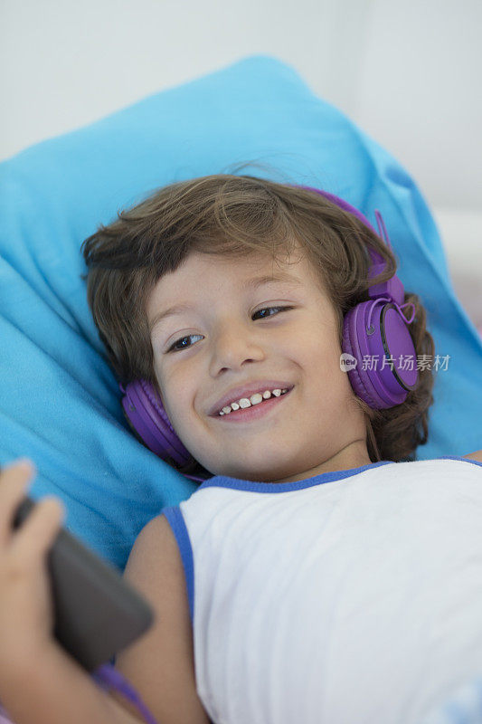 快乐的小男孩在家里用智能手机和耳机
