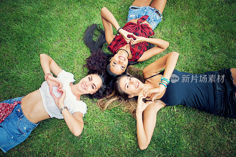 快乐的女友们躺在草地上用手做心形的肖像