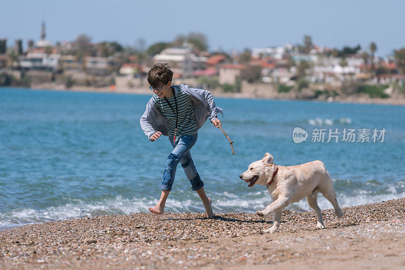 快乐的男孩和她的狗在沙滩上奔跑。