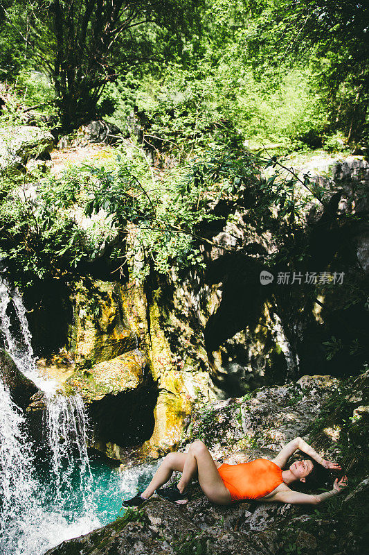 徒步旅行后，穿着泳衣的女人躺在瀑布附近的岩石上