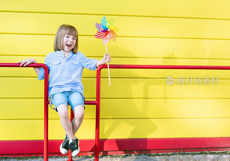 孩子拿着风车玩具站在黄色的墙前