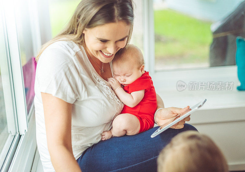 多任务拉美妈妈使用数字平板电脑与新婴儿和蹒跚学步