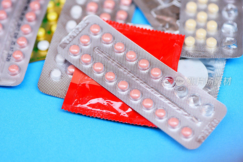蓝色背景上的避孕药片和避孕套——避孕药具是指预防怀孕或性传播疾病