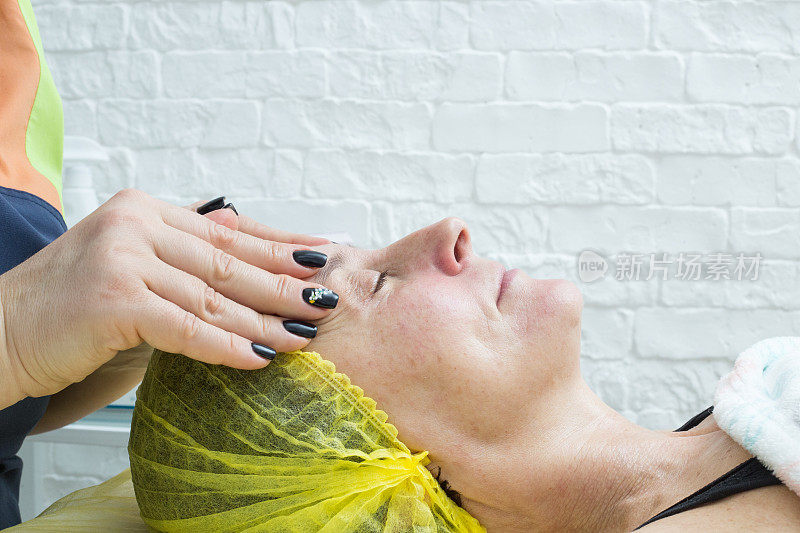 一个美容师的手按摩一个女人的脸，同时刷皮肤。