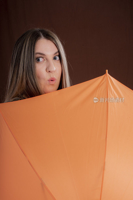 年轻女子拿着一把橙色的伞准备出门，看着镜头。