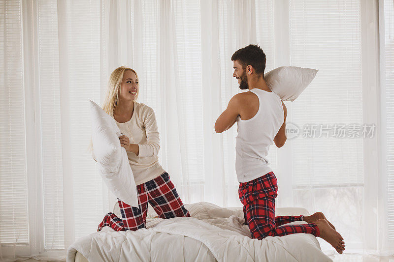 一对快乐的年轻夫妇在床上打枕头仗