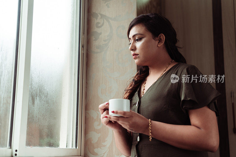 当喝热茶或咖啡时，体贴的女人在思考和看向别处