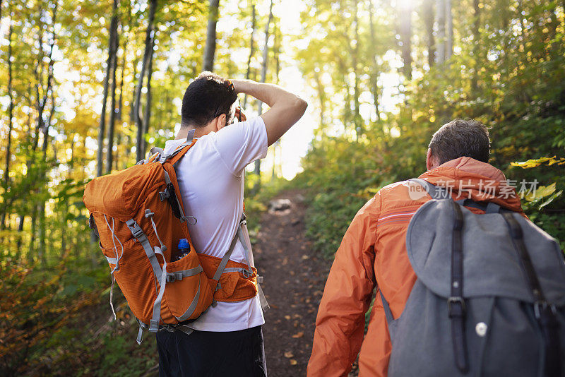 两名徒步旅行者在森林中向上移动，其中一人正在用相机拍下大自然的照片