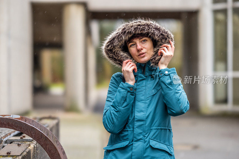 穿着蓝色雨衣的年轻女子在城市的混凝土环境中