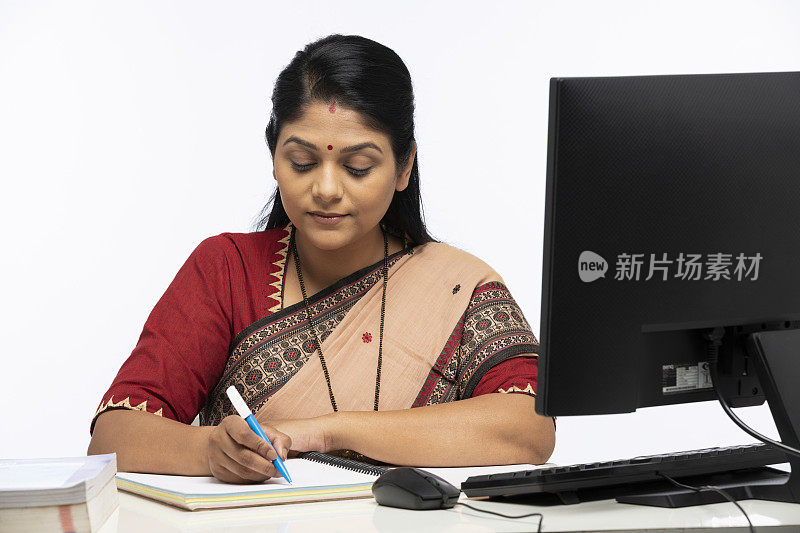 印度妇女的肖像作为一个教师在莎丽写在笔记本上。坐在孤立的白色背景:-库存照片