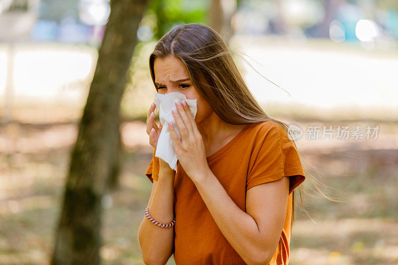季节性过敏的妇女用纸巾擤鼻子。