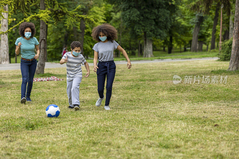 快乐的非裔美国家庭戴着防护口罩在公园里玩足球。