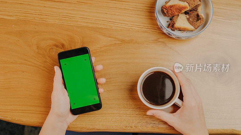 一名女子拿着咖啡杯，使用带有色度键绿色屏幕的智能手机