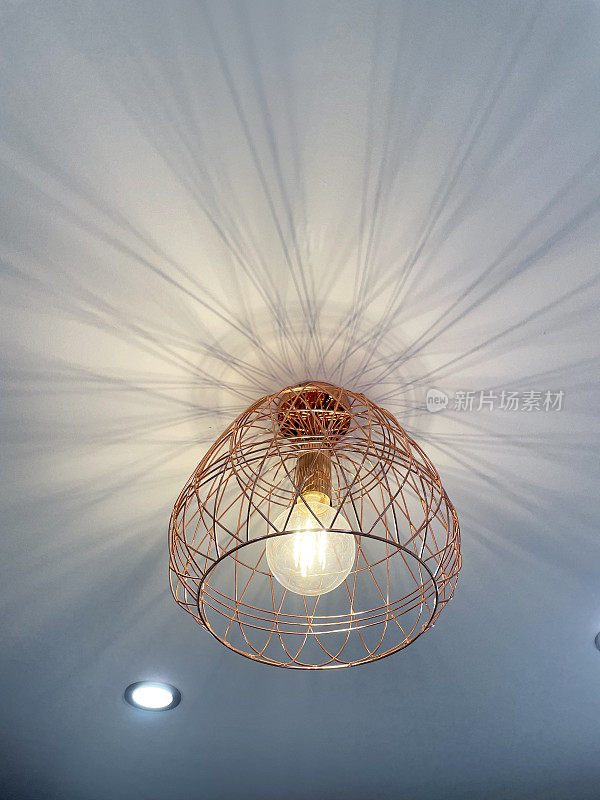 玫瑰金形象，铜篮灯罩悬挂在家庭房间的天花板上，由铜棒制成的几何形状灯罩，从下面看