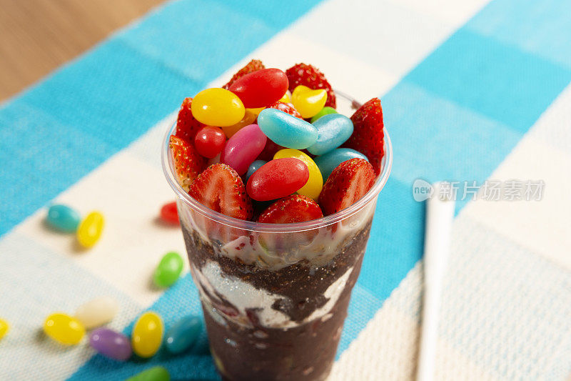 巴西巴西莓杯与草莓顶，炼乳和彩色果冻豆在白色和蓝色的背景，巴西莓冷冻近视图