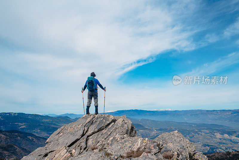 背景摄影师登山运动员是看风景，而持有登山杆在一个岩石山的顶峰。